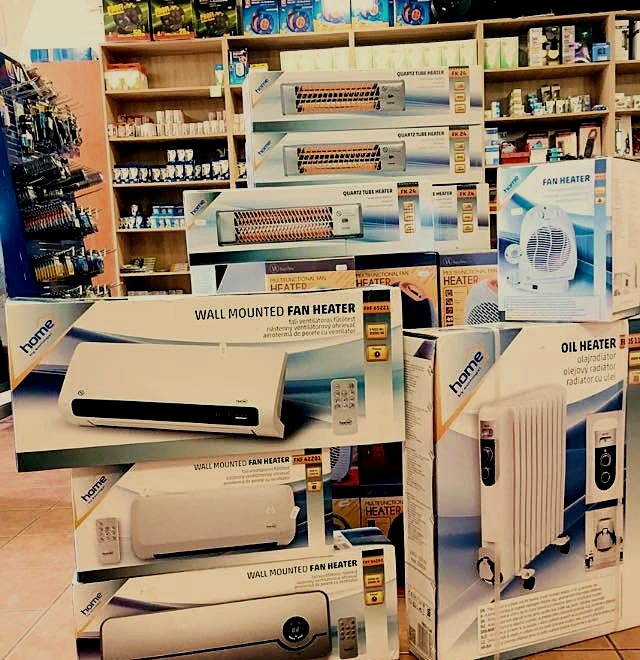 Fűtőtestek és ventilátorok dobozai a bolt padlóján, mögöttük teli polcfal.